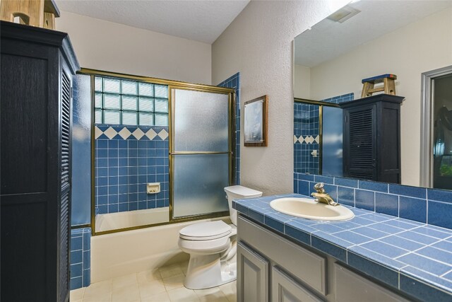 222 Winn Valley Dr, Wimberley, TX 78676 - bathroom with a textured wall, tile patterned flooring, vanity, toilet, and shower / bath combination with glass door