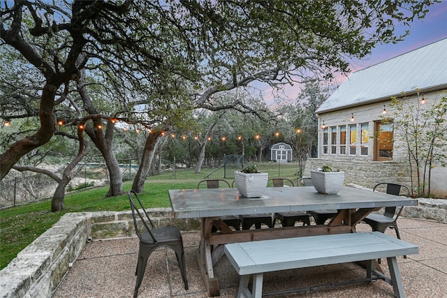 patio terrace at dusk featuring a storage unit and a lawn