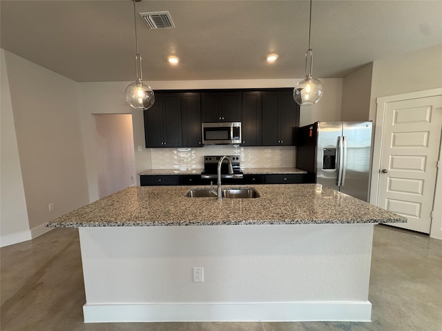 kitchen featuring appliances with stainless steel finishes, backsplash, sink, decorative light fixtures, and an island with sink