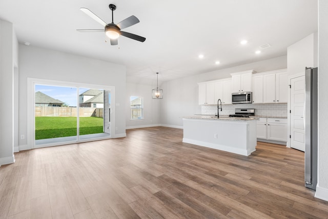 kitchen featuring backsplash, light stone counters, stainless steel appliances, a center island with sink, and white cabinets