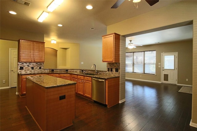 kitchen featuring sink, dishwasher, dark stone countertops, a kitchen island, and kitchen peninsula