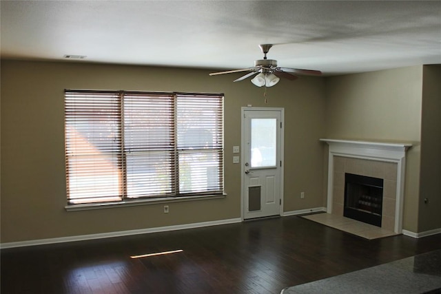 unfurnished living room featuring a tile fireplace, dark wood-type flooring, and ceiling fan