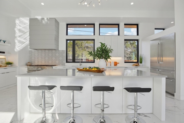 kitchen featuring stainless steel built in refrigerator, a breakfast bar area, backsplash, a large island, and white cabinets