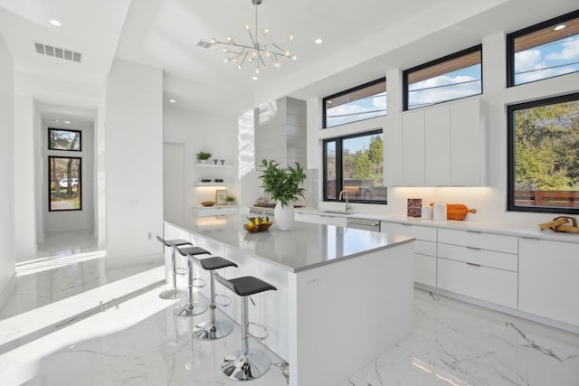 kitchen with a breakfast bar, white cabinetry, hanging light fixtures, a kitchen island, and a notable chandelier