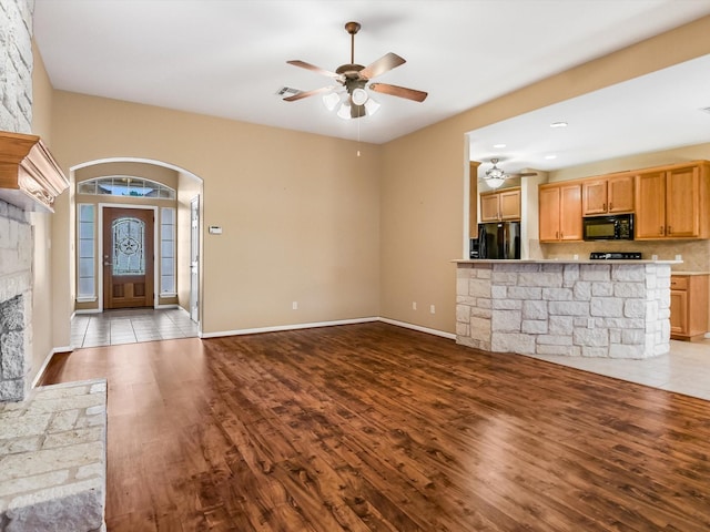 unfurnished living room with a stone fireplace, ceiling fan, and light wood-type flooring