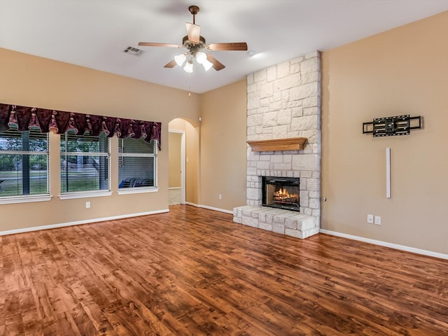 unfurnished living room with hardwood / wood-style flooring, a stone fireplace, and ceiling fan