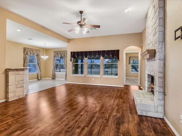 unfurnished living room featuring a wealth of natural light, a fireplace, hardwood / wood-style floors, and ceiling fan with notable chandelier