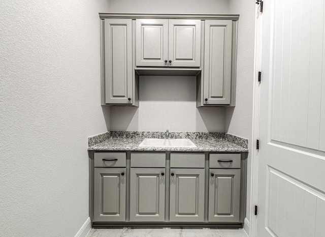 kitchen with light stone countertops, gray cabinets, and sink