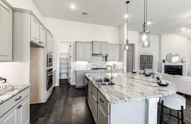 kitchen with gray cabinetry, sink, dark hardwood / wood-style floors, pendant lighting, and a center island with sink