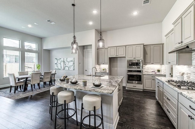 kitchen with decorative light fixtures, stainless steel appliances, a center island with sink, and sink