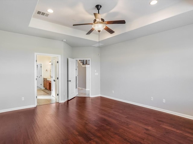 empty room with baseboards, visible vents, a ceiling fan, a raised ceiling, and wood finished floors