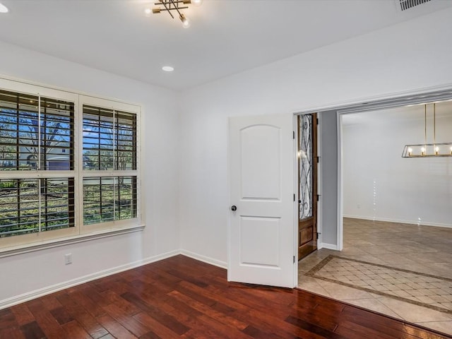 empty room featuring a notable chandelier, recessed lighting, hardwood / wood-style flooring, and baseboards