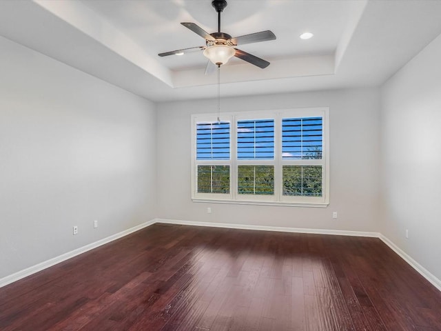 empty room featuring a ceiling fan, baseboards, a tray ceiling, and wood finished floors