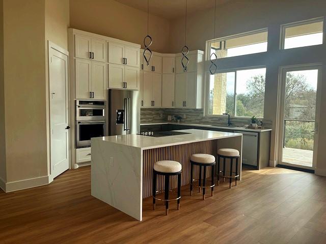 kitchen with white cabinetry, a center island, sink, stainless steel appliances, and pendant lighting