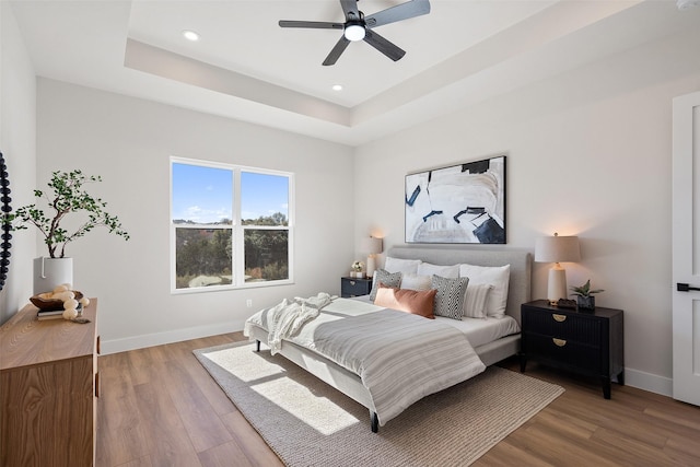 bedroom with hardwood / wood-style flooring, ceiling fan, and a tray ceiling