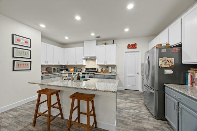 kitchen featuring white cabinets, gray cabinetry, stainless steel appliances, and an island with sink