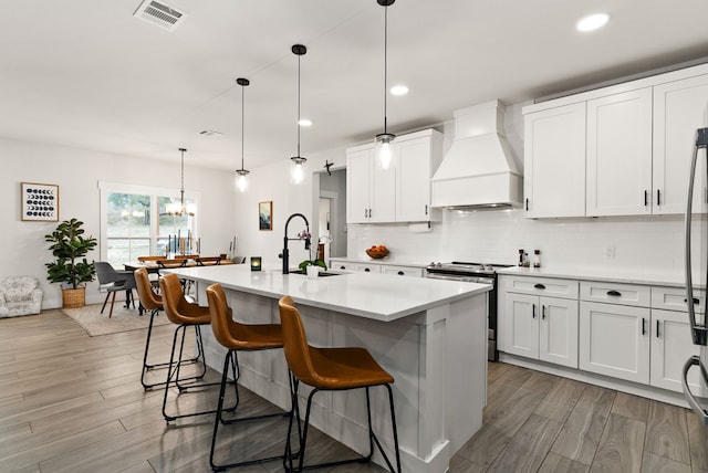 kitchen with white cabinetry, electric range, a center island with sink, and custom range hood