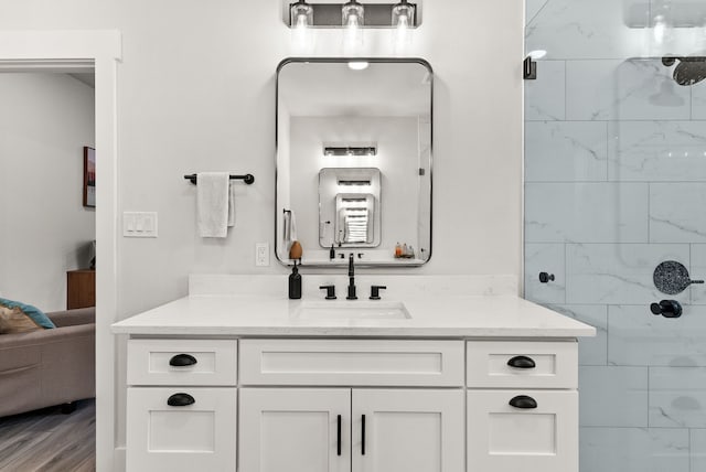 bathroom featuring a tile shower, vanity, and wood-type flooring