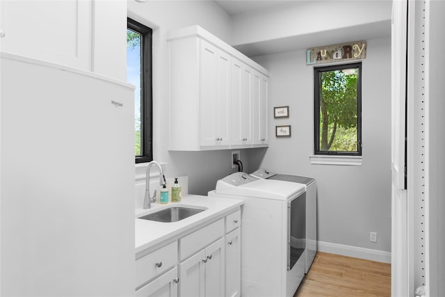 clothes washing area with light hardwood / wood-style floors, cabinets, sink, and washing machine and clothes dryer