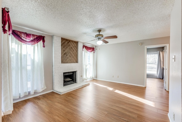 unfurnished living room with a textured ceiling, ceiling fan, hardwood / wood-style floors, and a brick fireplace