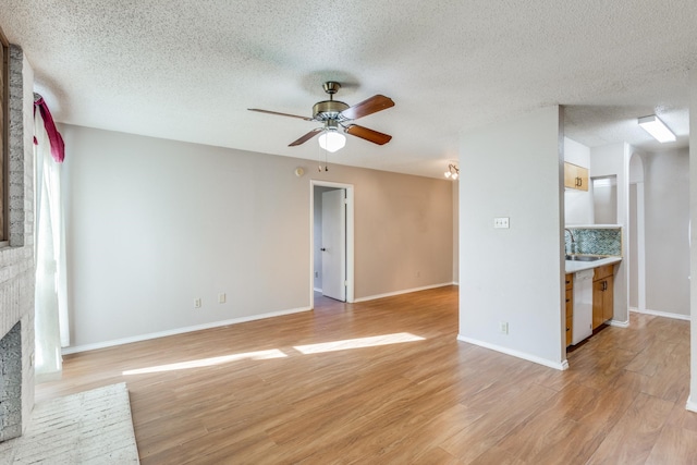 unfurnished living room with a brick fireplace, a textured ceiling, ceiling fan, and light wood-type flooring