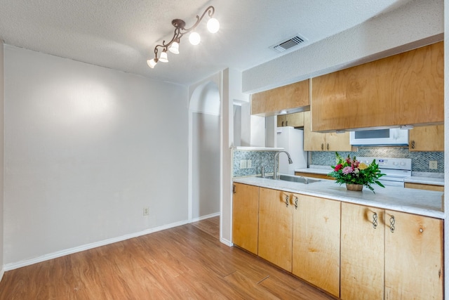 kitchen featuring tasteful backsplash, white appliances, a textured ceiling, light hardwood / wood-style flooring, and sink