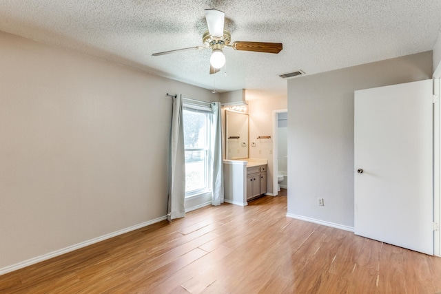 unfurnished bedroom with a textured ceiling, ceiling fan, ensuite bathroom, and light hardwood / wood-style floors