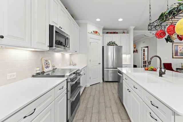 kitchen with decorative light fixtures, light wood-type flooring, white cabinets, appliances with stainless steel finishes, and sink