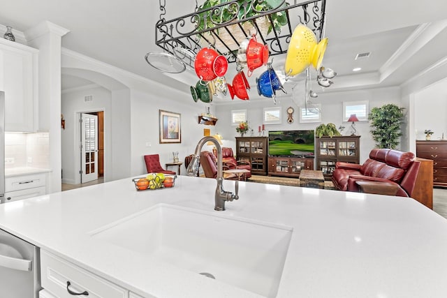 kitchen with dishwasher, a raised ceiling, white cabinets, ornamental molding, and sink