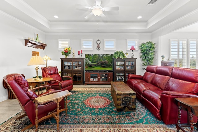 living room with a raised ceiling, ceiling fan, and ornamental molding