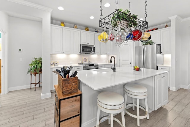 kitchen featuring appliances with stainless steel finishes, white cabinets, sink, and a center island with sink