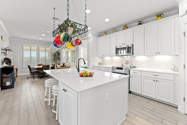 kitchen featuring stainless steel appliances, white cabinets, and an island with sink