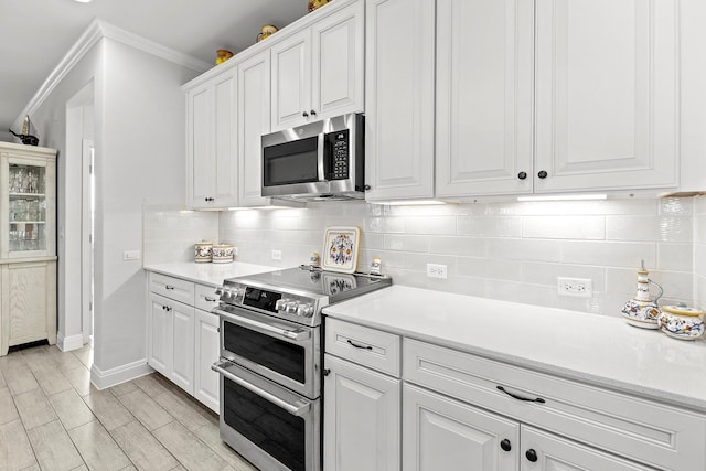 kitchen with white cabinets, tasteful backsplash, crown molding, and appliances with stainless steel finishes