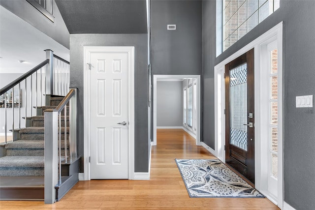 entryway featuring stairs, a towering ceiling, baseboards, and wood finished floors