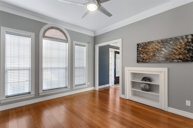 interior space with built in shelves, wood finished floors, a ceiling fan, baseboards, and ornamental molding