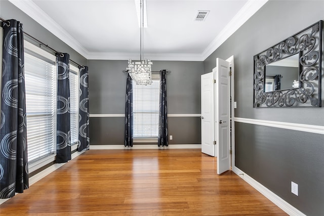 unfurnished dining area featuring a notable chandelier, wood finished floors, visible vents, baseboards, and ornamental molding