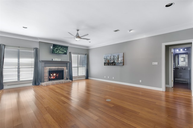 unfurnished living room featuring a brick fireplace, ceiling fan, crown molding, and wood-type flooring