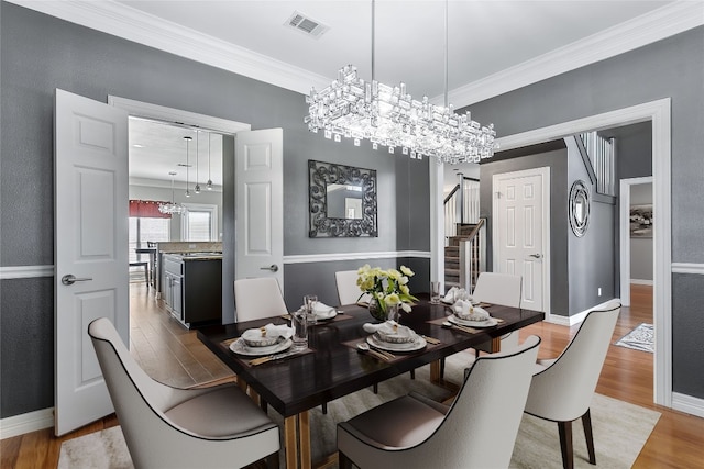 dining space with light wood-type flooring, visible vents, crown molding, and stairs