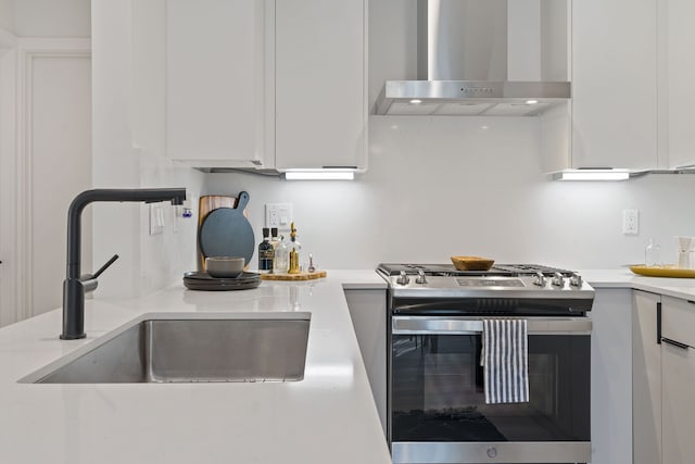 kitchen with white cabinets, wall chimney range hood, stainless steel range with gas stovetop, and sink