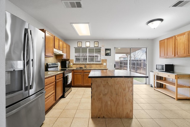 kitchen featuring sink, a center island, light tile patterned flooring, backsplash, and appliances with stainless steel finishes