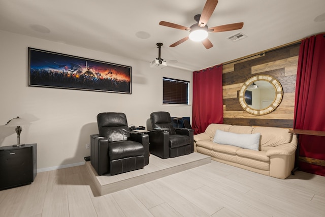 home theater room featuring ceiling fan, light hardwood / wood-style floors, and wooden walls