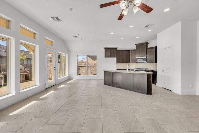 kitchen with a center island with sink, light tile patterned floors, decorative backsplash, dark brown cabinets, and lofted ceiling