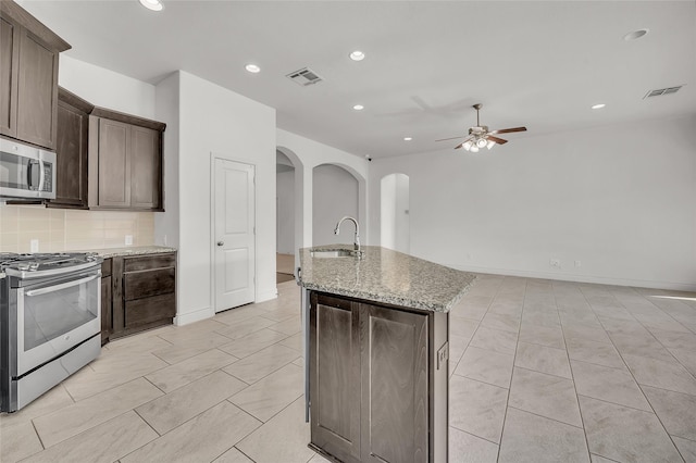 kitchen featuring stainless steel appliances, sink, ceiling fan, tasteful backsplash, and an island with sink