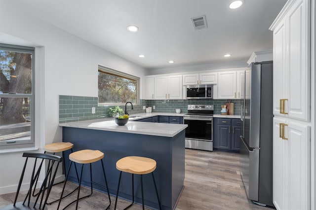 kitchen featuring white cabinets, light hardwood / wood-style flooring, kitchen peninsula, a breakfast bar area, and appliances with stainless steel finishes