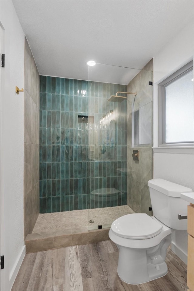 bathroom featuring toilet, tiled shower, and wood-type flooring