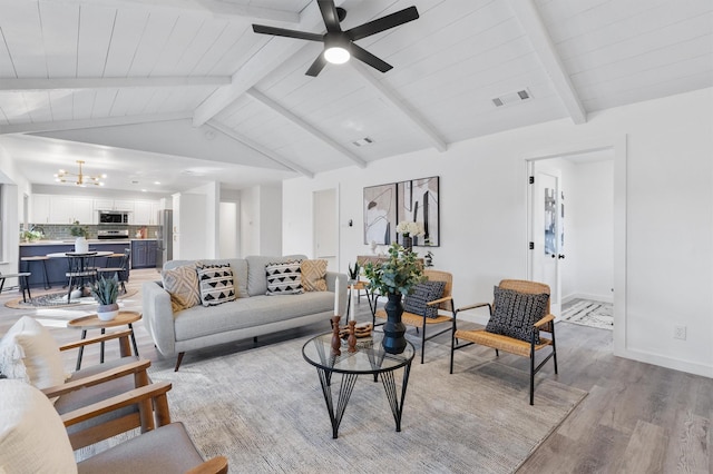 living room with ceiling fan with notable chandelier, light hardwood / wood-style flooring, and vaulted ceiling with beams