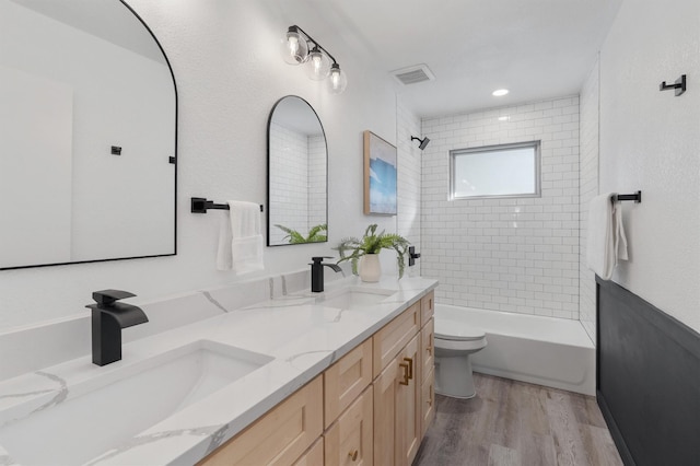 full bathroom featuring wood-type flooring, tiled shower / bath combo, vanity, and toilet