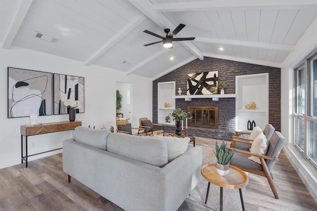 living room with ceiling fan, a brick fireplace, vaulted ceiling with beams, and wood-type flooring