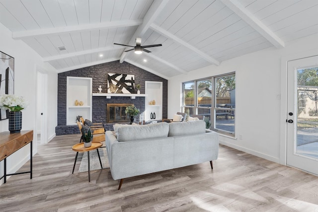 living room featuring ceiling fan, light hardwood / wood-style flooring, a brick fireplace, and lofted ceiling with beams