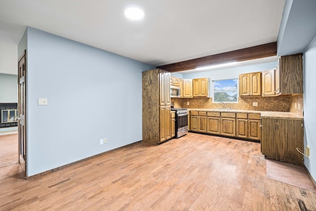 kitchen featuring appliances with stainless steel finishes, light wood-type flooring, beam ceiling, sink, and tasteful backsplash